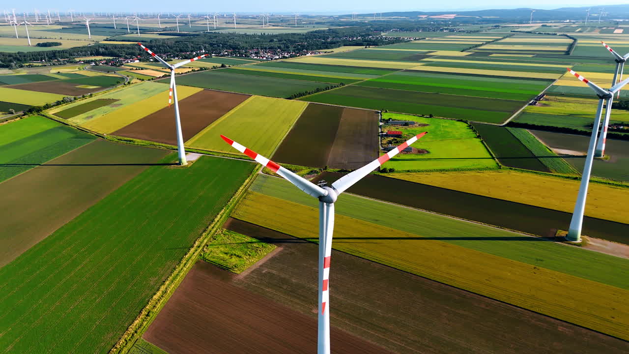 Towers rise above green fields. Aerial view showcasing wind turbines above expansive farmland and vibrant green fields under a bright sky