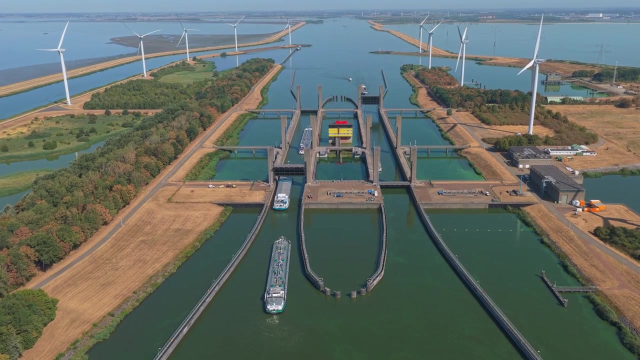 Impresionante perspectiva aérea de las esclusas de Kreekrak en los Países Bajos, mostrando buques de carga navegando por el sistema de canales con aerogeneradores cerca.