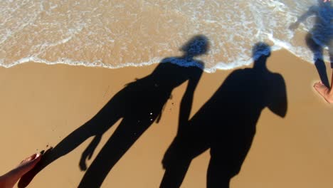 Shadow-of-a-couple-holding-hands-as-they-walk-down-a-beach-towards-the-water-at-a-tropical-Brazilian-beach-in-Rio-Grande-do-Norte,-Brazil