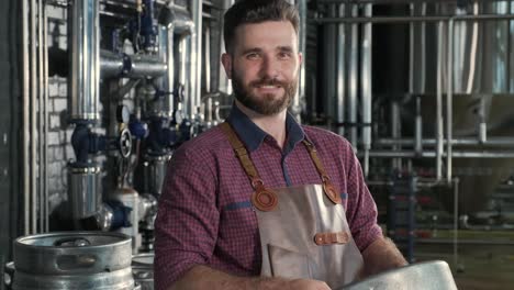 young brewer wearing leather apron holds a barrel with craft beer at a modern brewery