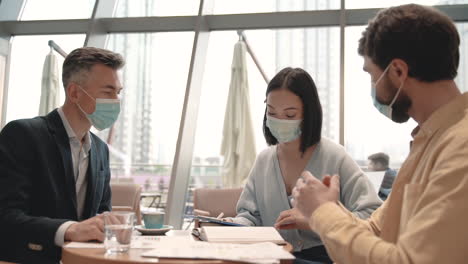 a work team with masks discusses details of some data in a report in the coffee shop