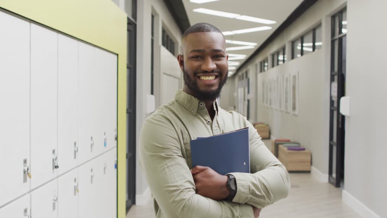 video de un feliz maestro afroamericano de pie en el pasillo de la escuela