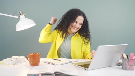 una mujer joven mira la computadora portátil y se alegra.