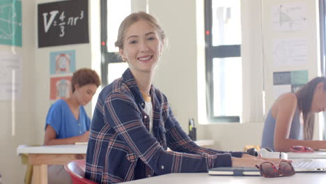 in high school, teenage girl smiling and sitting at desk in classroom