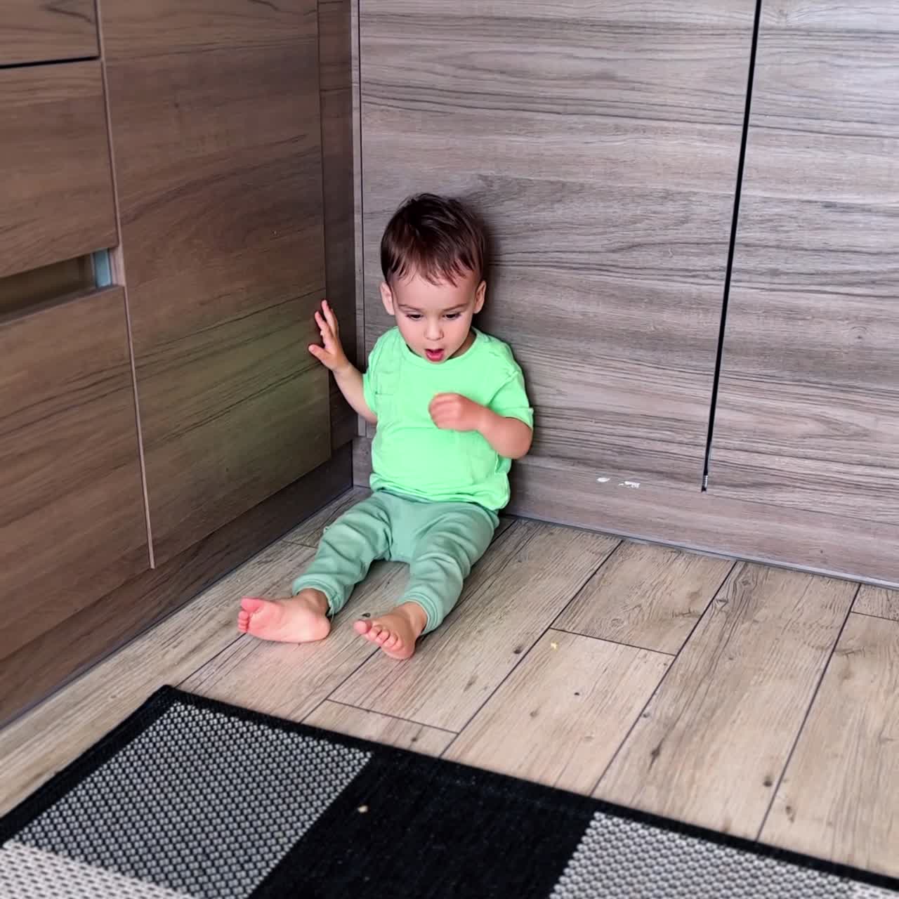 One year old toddler sitting on the kitchen shoving his feet cheerfully. Kid eating a snack. Vertical video