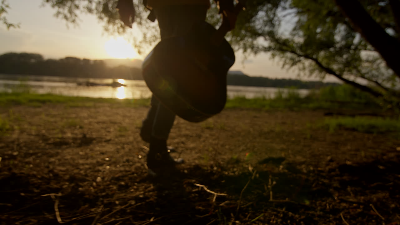Musician Walking Along a Riverbank at Sunset