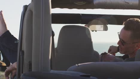 Happy-caucasian-gay-male-couple-in-car-relaxing-with-feet-out-of-window-on-sunny-day-at-the-beach