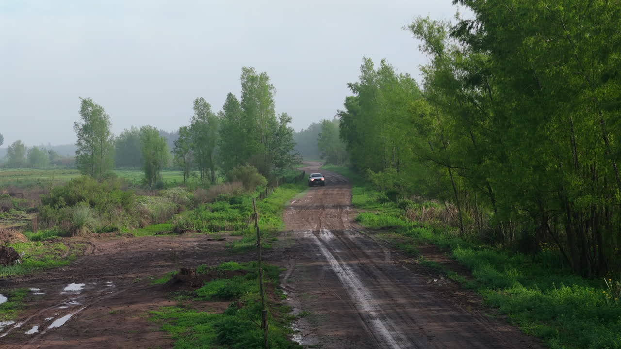 Drone approach to van driving on rural dirt road flanked by forest in the Argentine Delta
