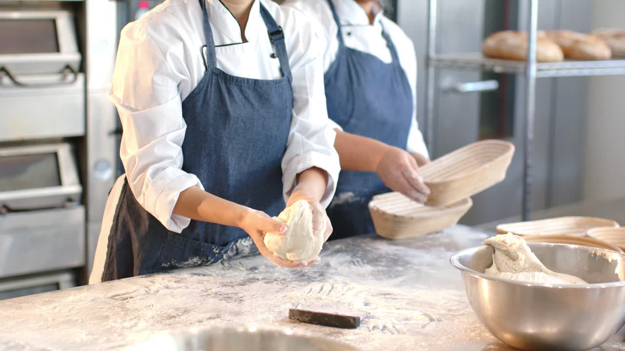 Kvinnelige bakere løfter deig fra bolle på melet arbeidsbenk, skraper med skrape, former for heving.