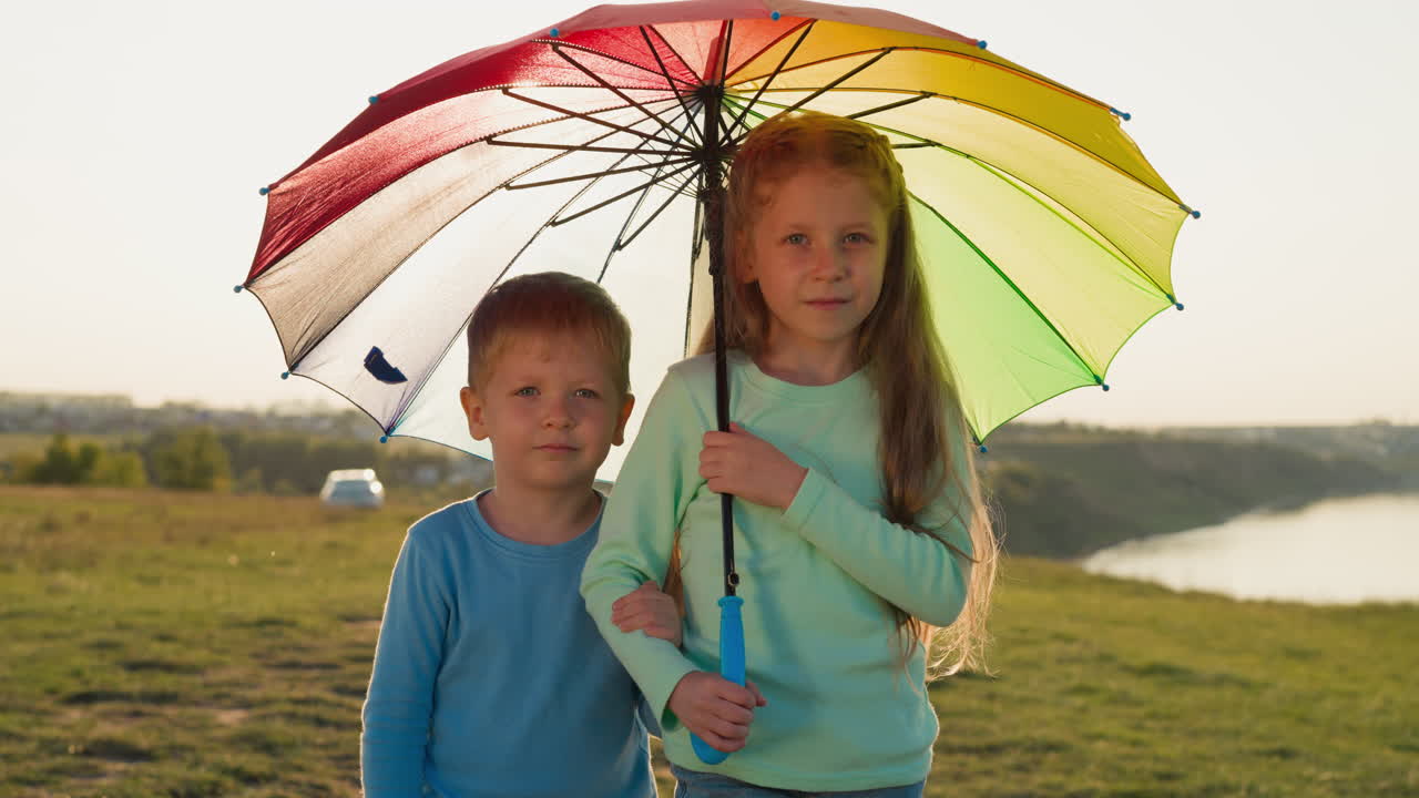 Children under umbrella at riverside on rainy day cute little brother and sister hide together under