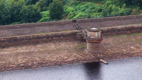 Camera slowly pans across a stone control tower on a masonry dam at a historic reservoir, with lush greenery and overcast natural lighting