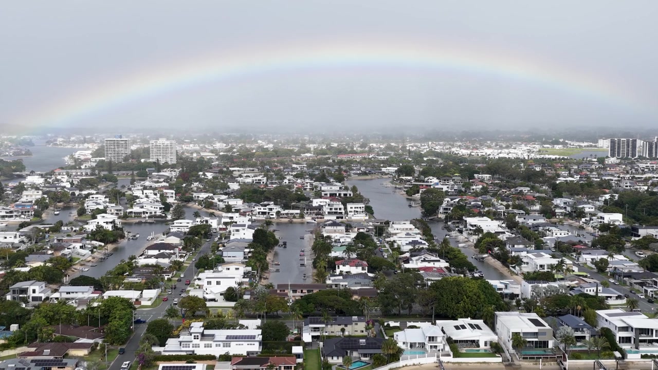 Ampia ripresa aerea di un arcobaleno che si inarca su lussuose case sul canale sotto cieli coperti