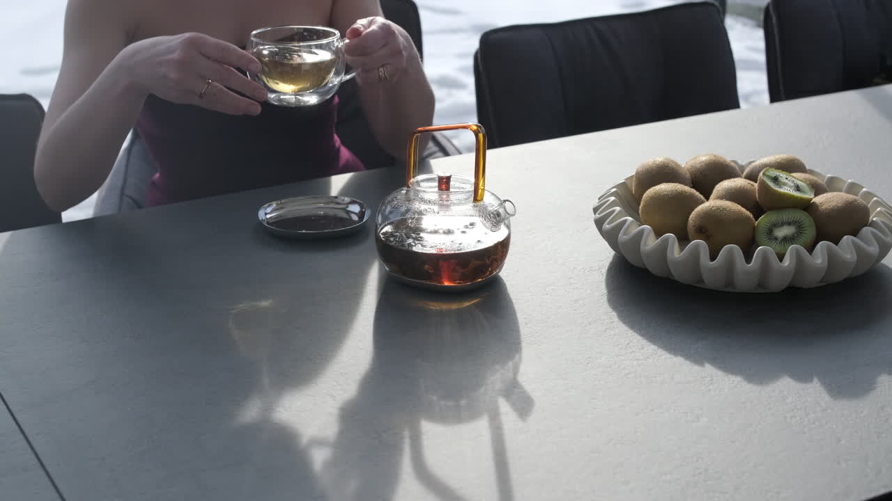 Donna che versa e beve tè a un tavolo con kiwi