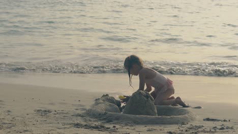 una chica linda con trenzas construye un castillo de arena en la playa de la noche