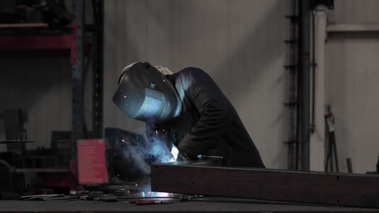 Industrial Worker In Protective Mask And Suit Welding Metal In A Factory - medium shot