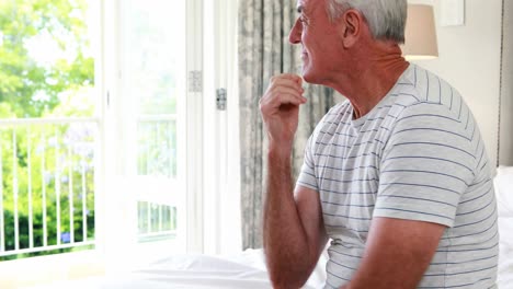 Worried-senior-man-sitting-on-bed-in-bedroom