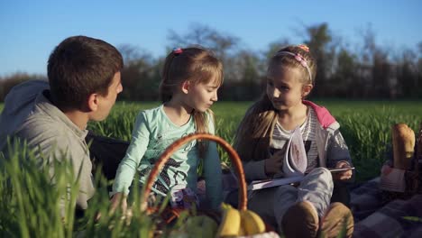 beautiful, windy day. father with two daughters are having a picnic on a green field. little girl is feeding her dad with a cookie. close up