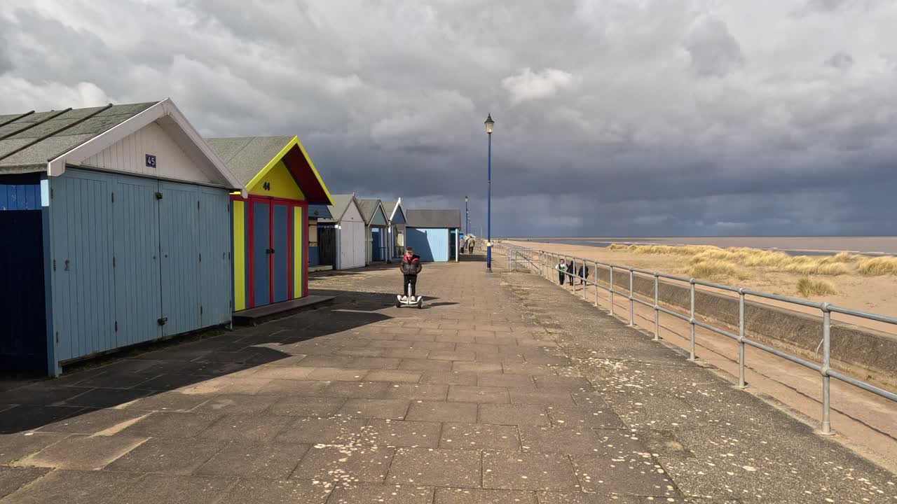 Colorful beach huts stood in a line along the seafront with sandy beach and moody grey sky&rsquo;s
