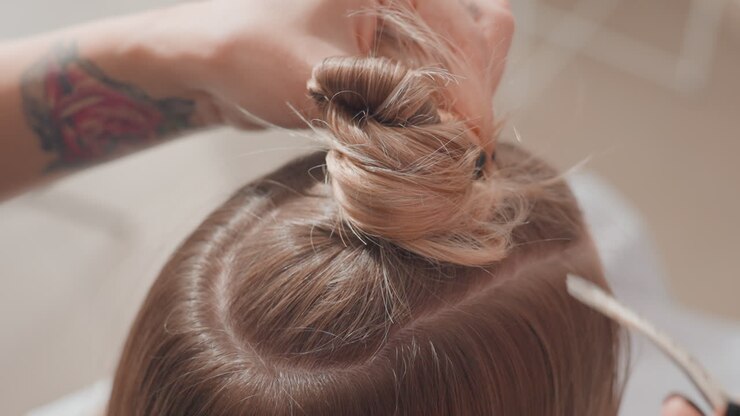 primo piano parrucchiere del salone acconciatura capelli divisi chignon parrucchiere arrotola e fissa ciocche di capelli biondi castani divisi in uno chignon ordinato, linee di divisione precise, clip e forcina usate, mani concentrate, studio soft