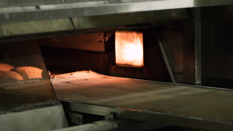 a baker placing the raw dough buns inside a pre-heated deck oven using a loader belt - baking bread in a bakery - closeup shot