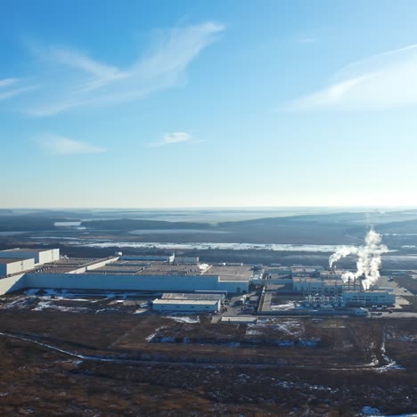 industrial factory in environment under blue sky. manufacturing among nature in winter. white smoke coming out of pipes into the air. aerial view.