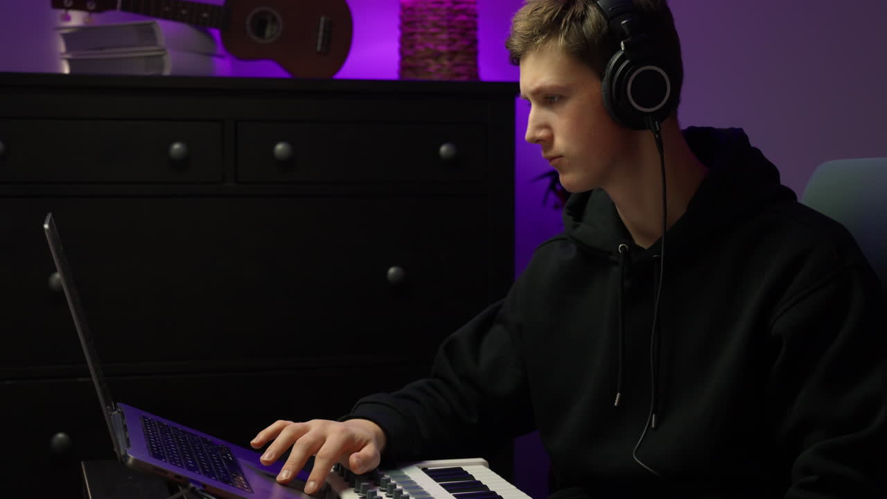 Young man in home studio producing music on laptop with headphones
