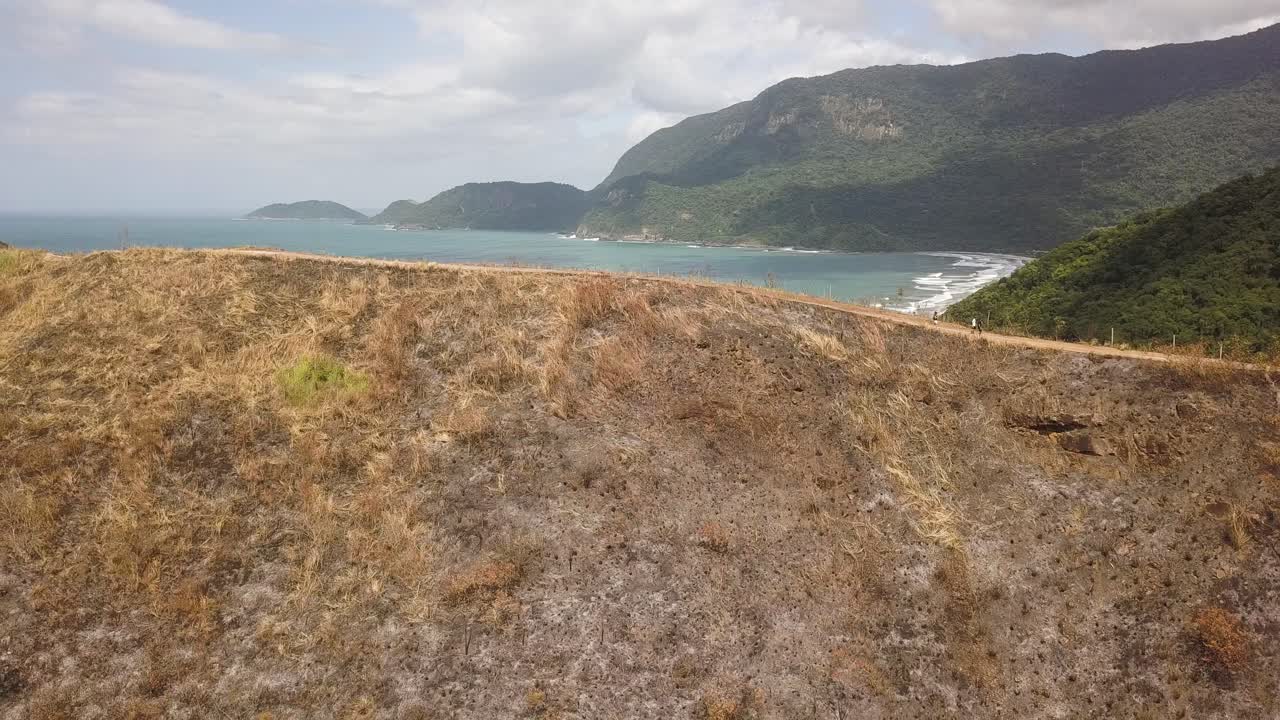 Unrecognizable people walking on dirt road over mountain after fire. Aerial backwards