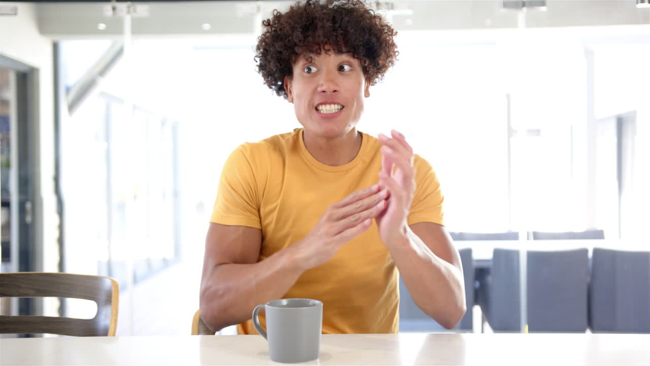 Surprised man in yellow shirt reacting while sitting at table with coffee mug