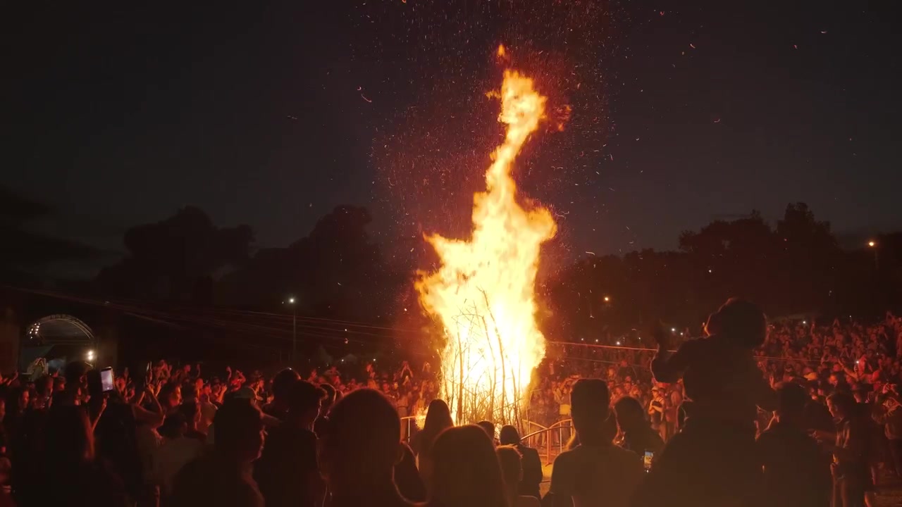 Folk står omkring et stort bål på en festival.