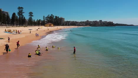 tourists swimming in ocean waves at beach during surf lesson, manly, sydney, australia
