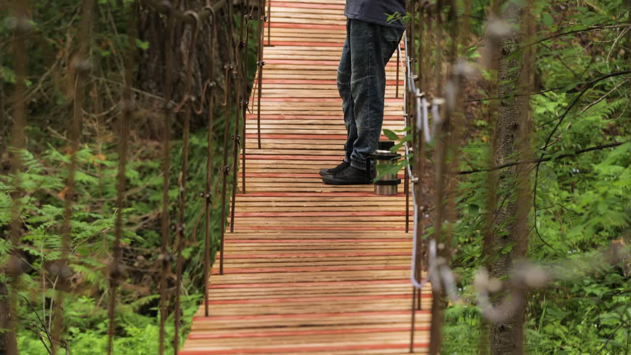 hombre caminando en un puente colgante de madera en un bosque