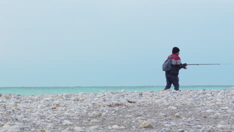 Fischer-Mit-Rucksack-Wirft-Seine-Angelrute-Ins-Meer-Und-Spaziert-An-Einem-Sonnigen-Morgen-Entlang-Der-Steinigen-Küste