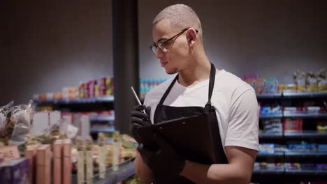 salesman in apron using tablet counting goods in supermarket, regular inventory to control goods