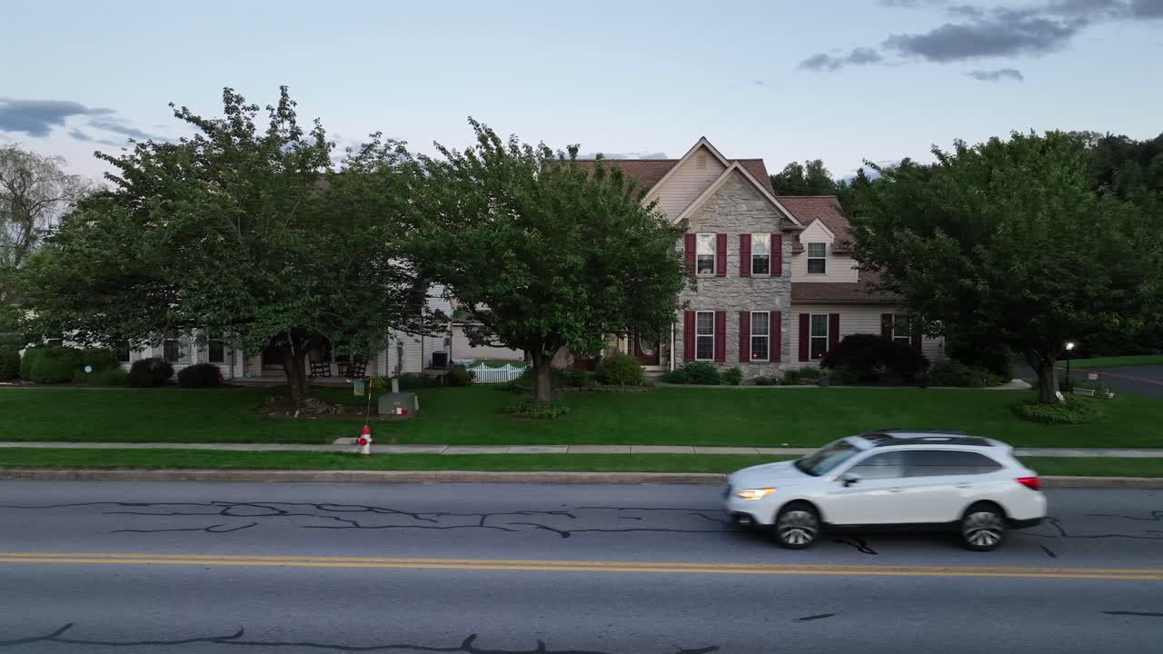 American brick house with car on street in American town. Aerial lateral shot. Sunset time in American suburbia.
