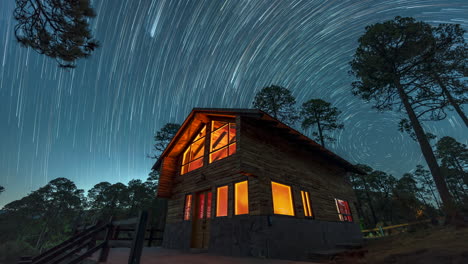 long exposure of star trails swirling over a warmly lit wooden cabin surrounded by pine trees in a tranquil forest. timelapse video