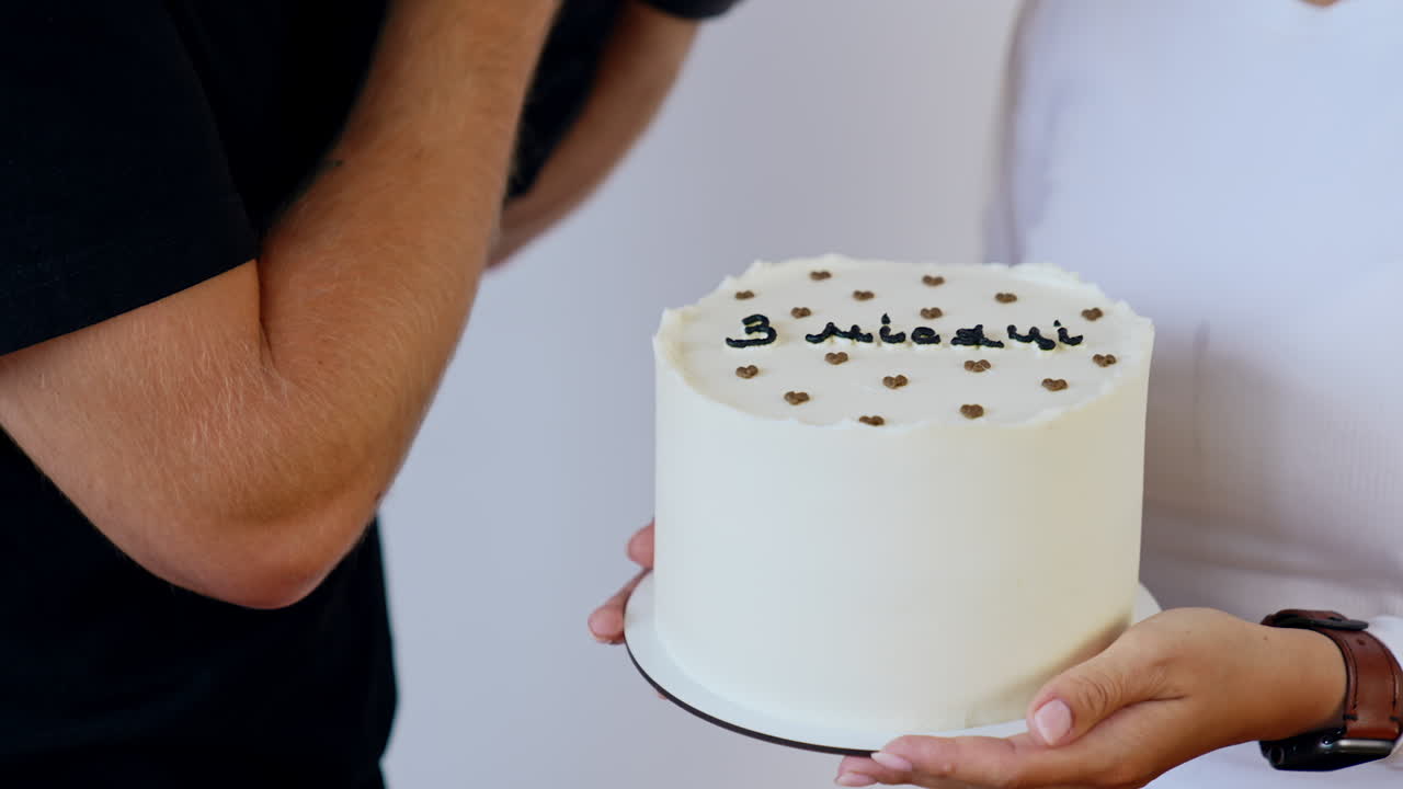 White cake with a black sign "three months" on in the female hands. Man holds a baby near the cake.