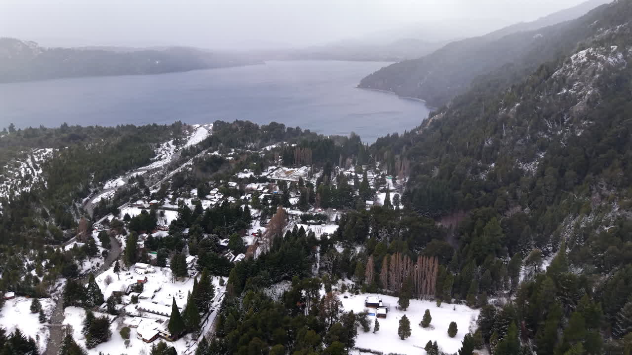 Winter scene of snow-covered houses beside a vast frozen lake, surrounded by a serene snowy landscape.Colonia Suiza, Bariloche, Argentina