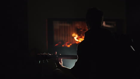 Ein-Junger-Mann-Spielt-Gitarre,-Allein-Am-Kamin-Sitzend