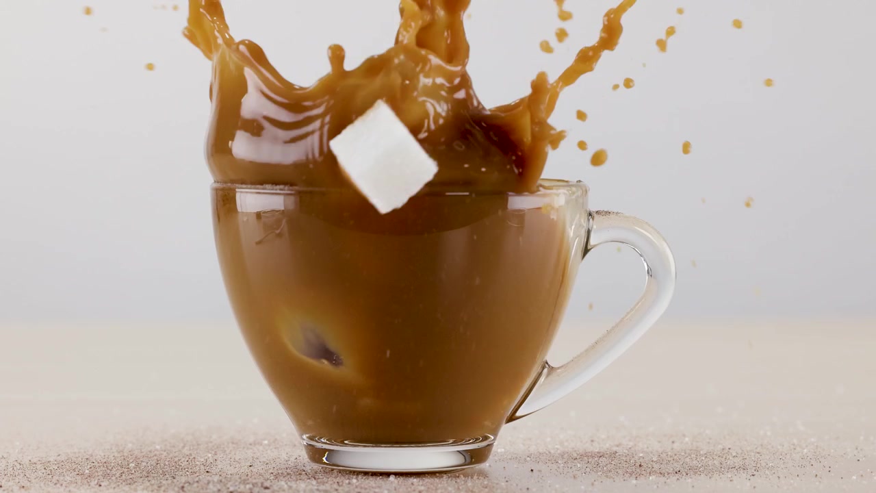 Spruzzo al rallentatore mentre un cubetto di zucchero cade in una tazza di vetro di caffè macchiato