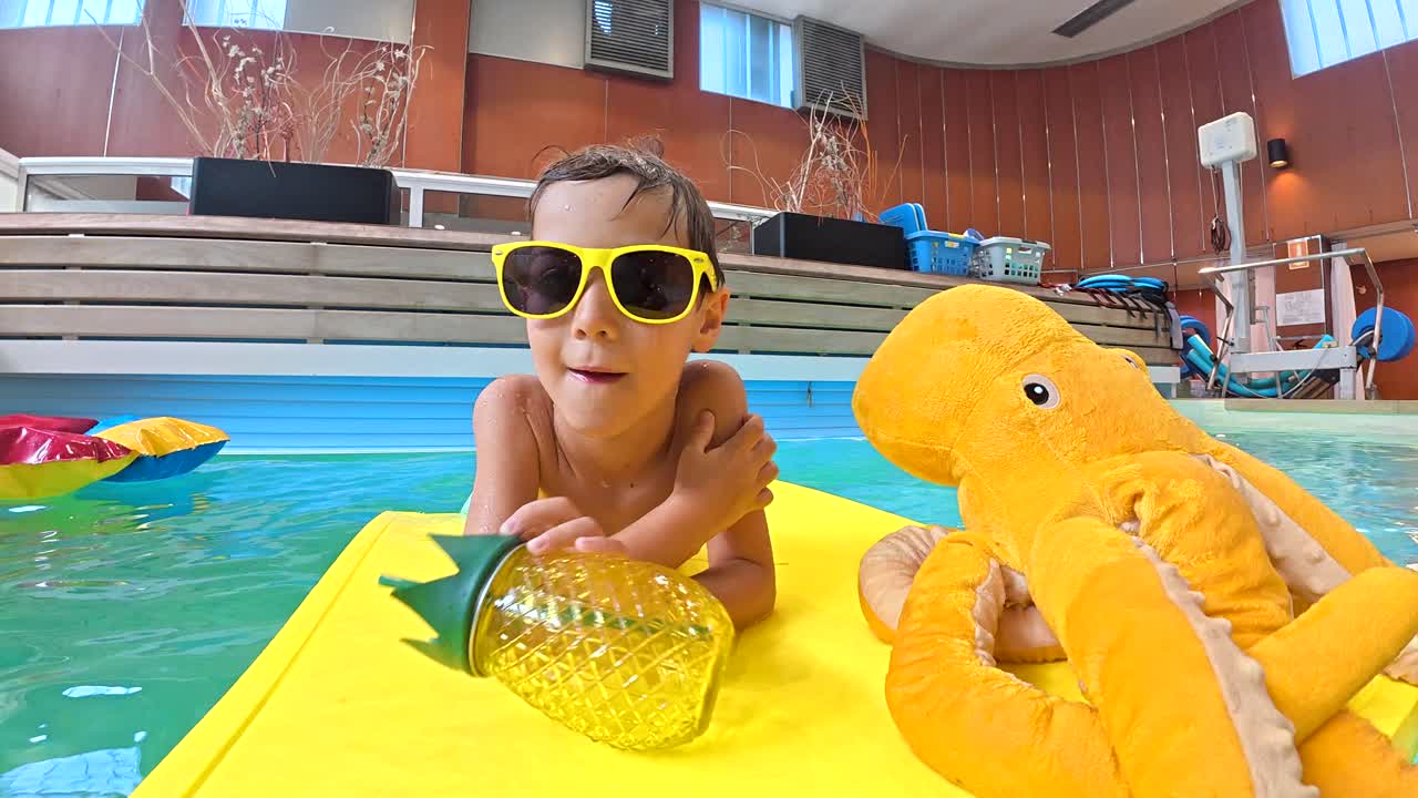 Boy with pineapple cup and toy octopus in swimming pool