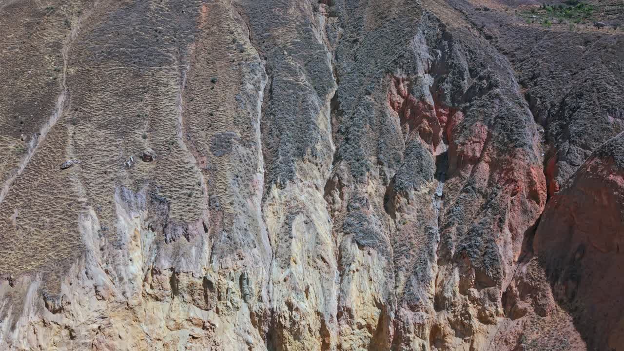 En drönare stiger över basen av Colca Canyon, Peru, och avslöjar livfulla rödorangea och gula sedimentlager, vattenutmejslade gångar och detaljer om erosion är tydligt synliga, vilket framhäver geologiska mönster