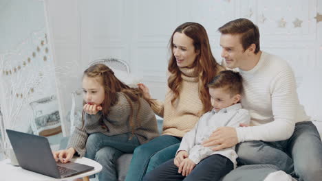 familia feliz sentada cerca de la computadora portátil en una casa de lujo