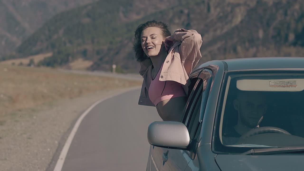 una dama rubia alegre se sienta con la mano levantada en la ventana del coche