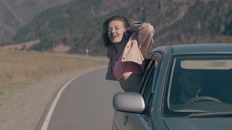 joyful-blonde-lady-sits-with-raised-hand-on-car-window