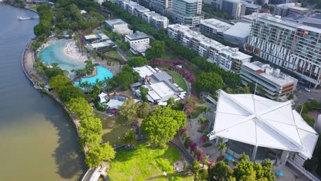 sunlight breaks between clouds casting light on park and pool next to brisbane river