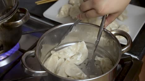 dumplings al vapor en vapor de metal sobre la olla en la estufa, mano con pinzas sirviendo