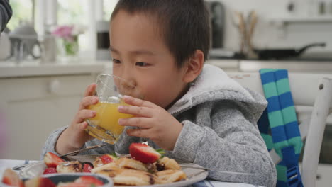 cute little asian boy drinking juice eating waffles for breakfast enjoying healthy homemade meal with family in kitchen at home 4k