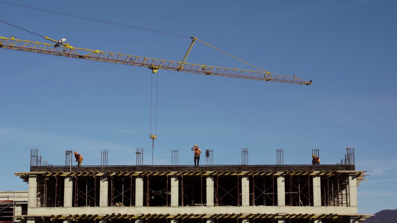 Tower crane bringing materials to workers on last flat of building installing - fabricating ground beam timber of construction site