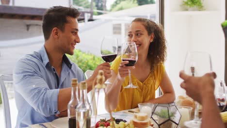 Two-diverse-male-and-female-friends-toasting-with-wine-at-dinner-party-on-patio