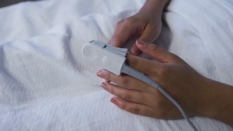 mixed race female patient lying in bed wearing fingertip pulse oximeter